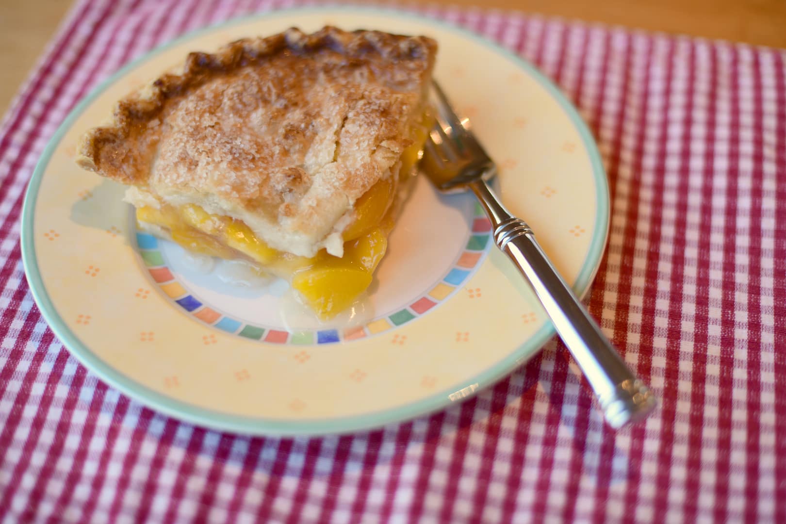 A piece of peach pie sits on a plate with a fork.